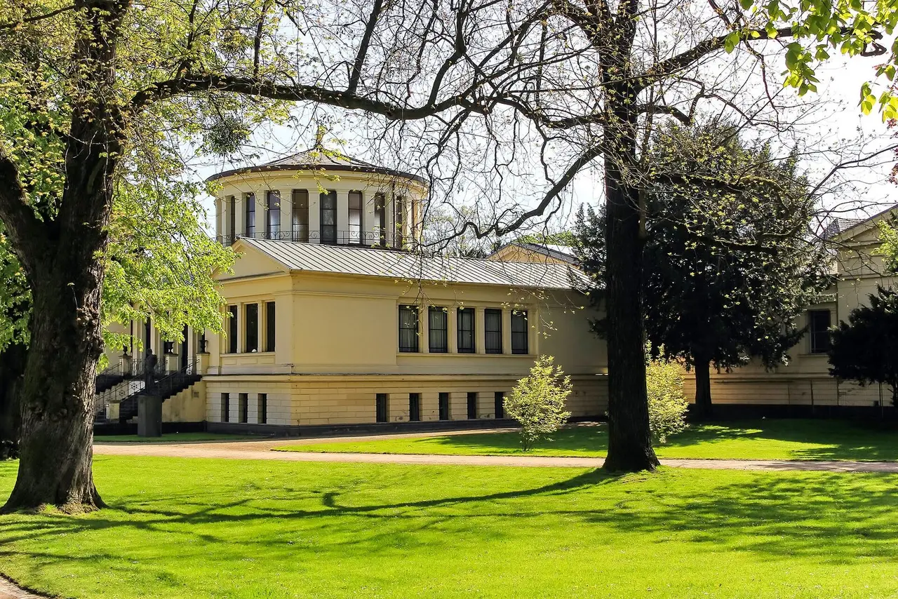 Klassizistischer gelber Museumsbau mit Rundbau des Akademischen Kunstmuseums hinter Bäumen am Hofgarten