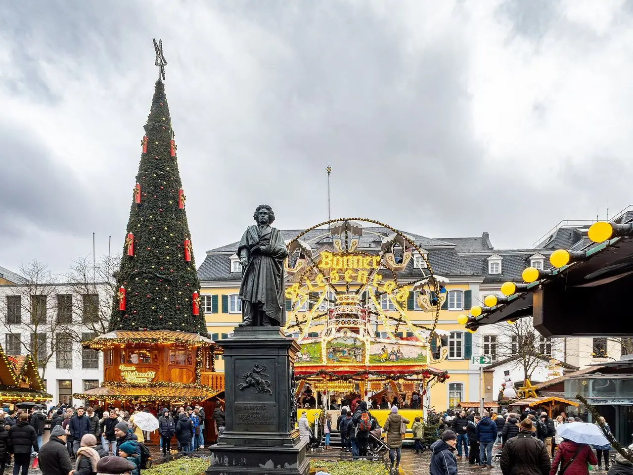 Bonner Weihnachtsmarkt auf dem Münsterplatz mit großem Weihnachtsbaum, Beethoven-Denkmal, Riesenrad und Besuchern vor der Alten Post