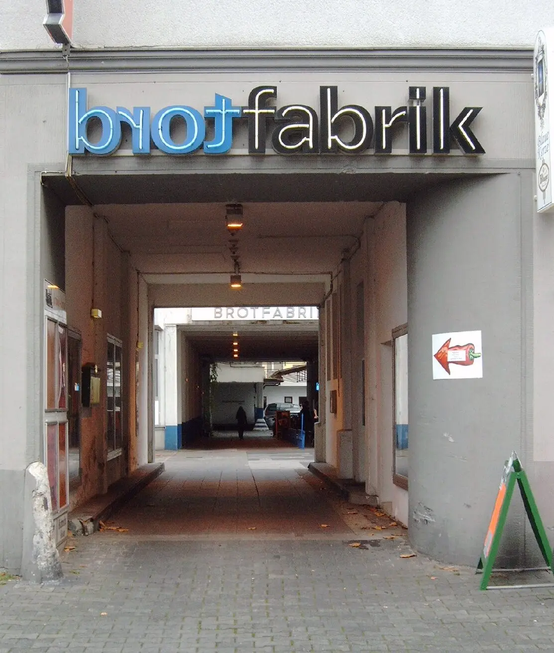 Toreinfahrt an der Kreuzstraße mit dem Schriftzug „brotfabrik“ und Durchgang zum Innenhof
