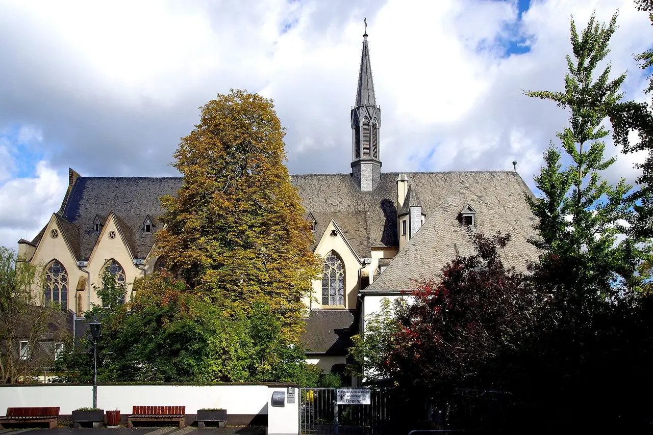 Gotische Christuskirche mit schlankem Dachreiter hinter herbstlichen Bäumen in Andernach