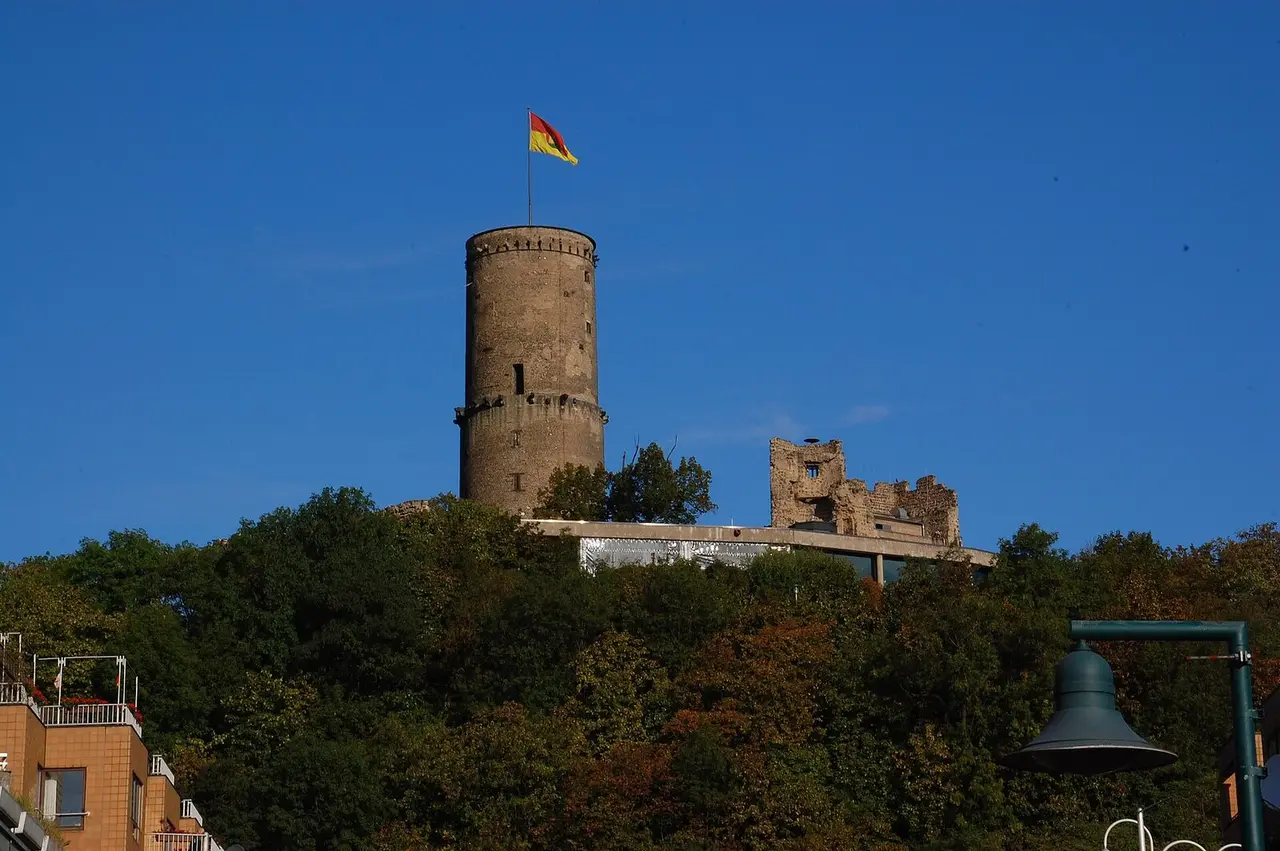 Runder Bergfried mit Fahne und Burgruine auf dem bewaldeten Godesberg über Bad Godesberg