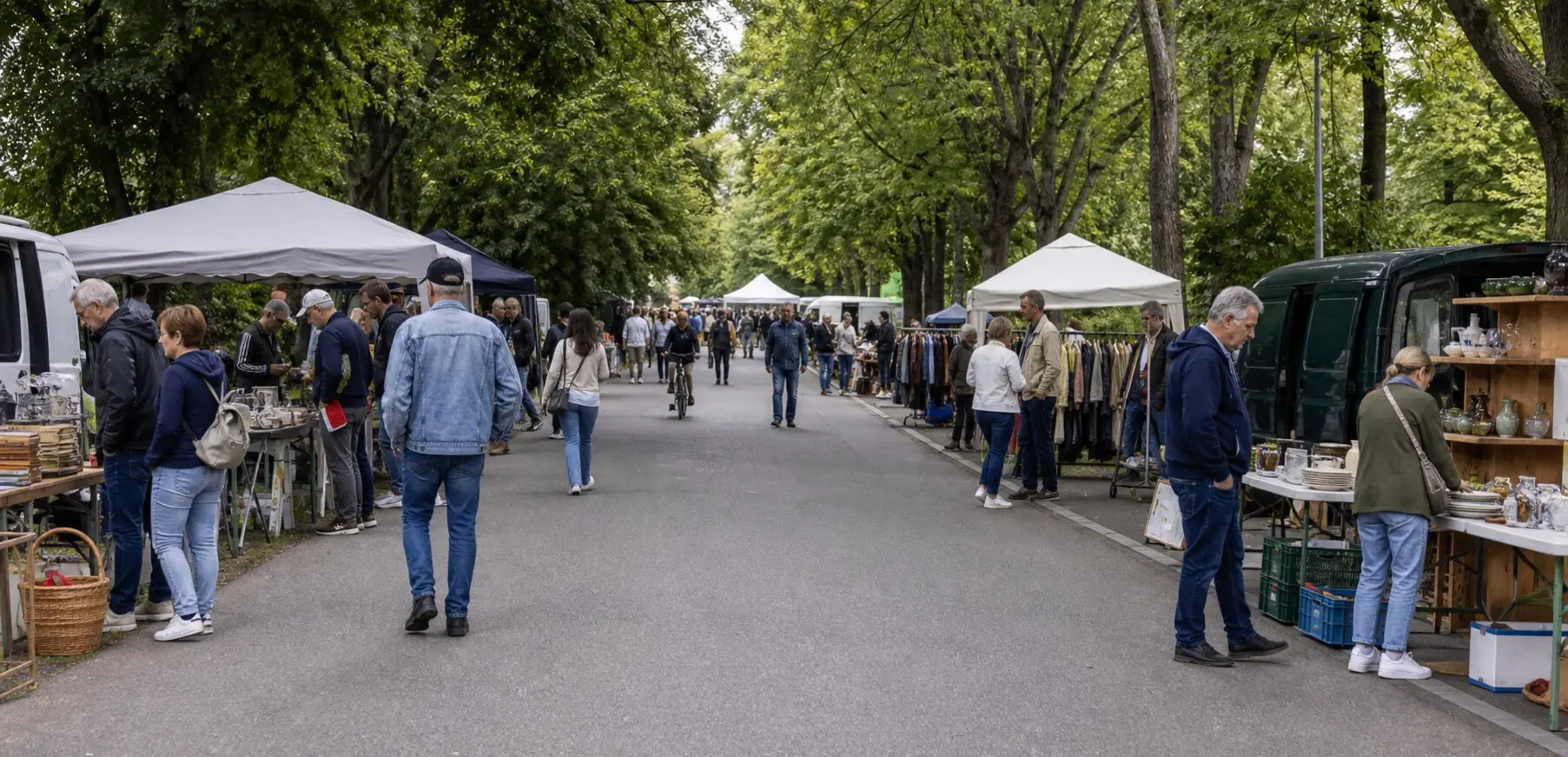 Flohmarktstände und Besucher säumen eine asphaltierte Fahrradstraße in der grünen Rheinaue