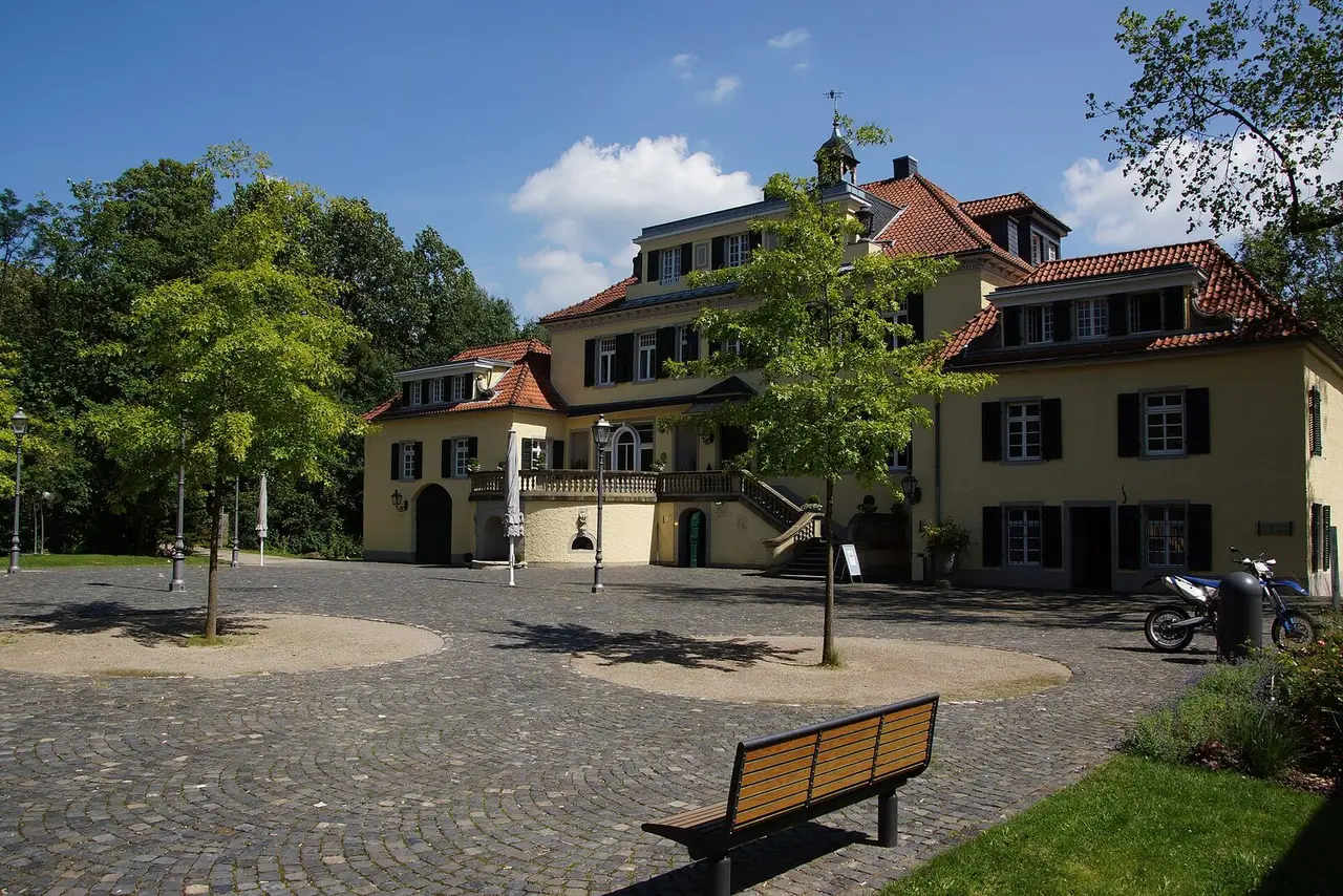 Herrenhaus von Schloss Eulenbroich mit Türmchen hinter gepflastertem Hof und Bäumen