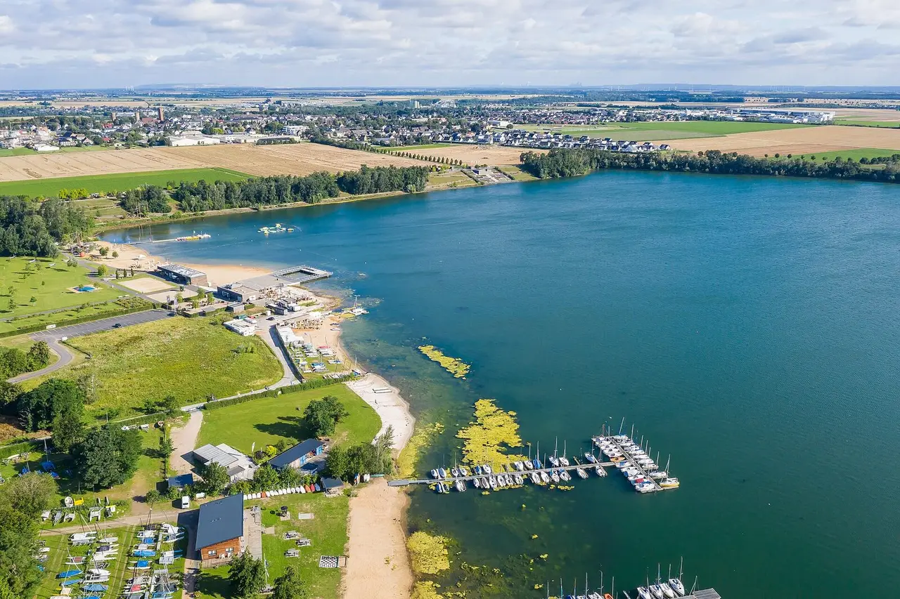 Luftaufnahme des Wassersportsees mit Strand, Stegen und Grünflächen im Seepark Zülpich