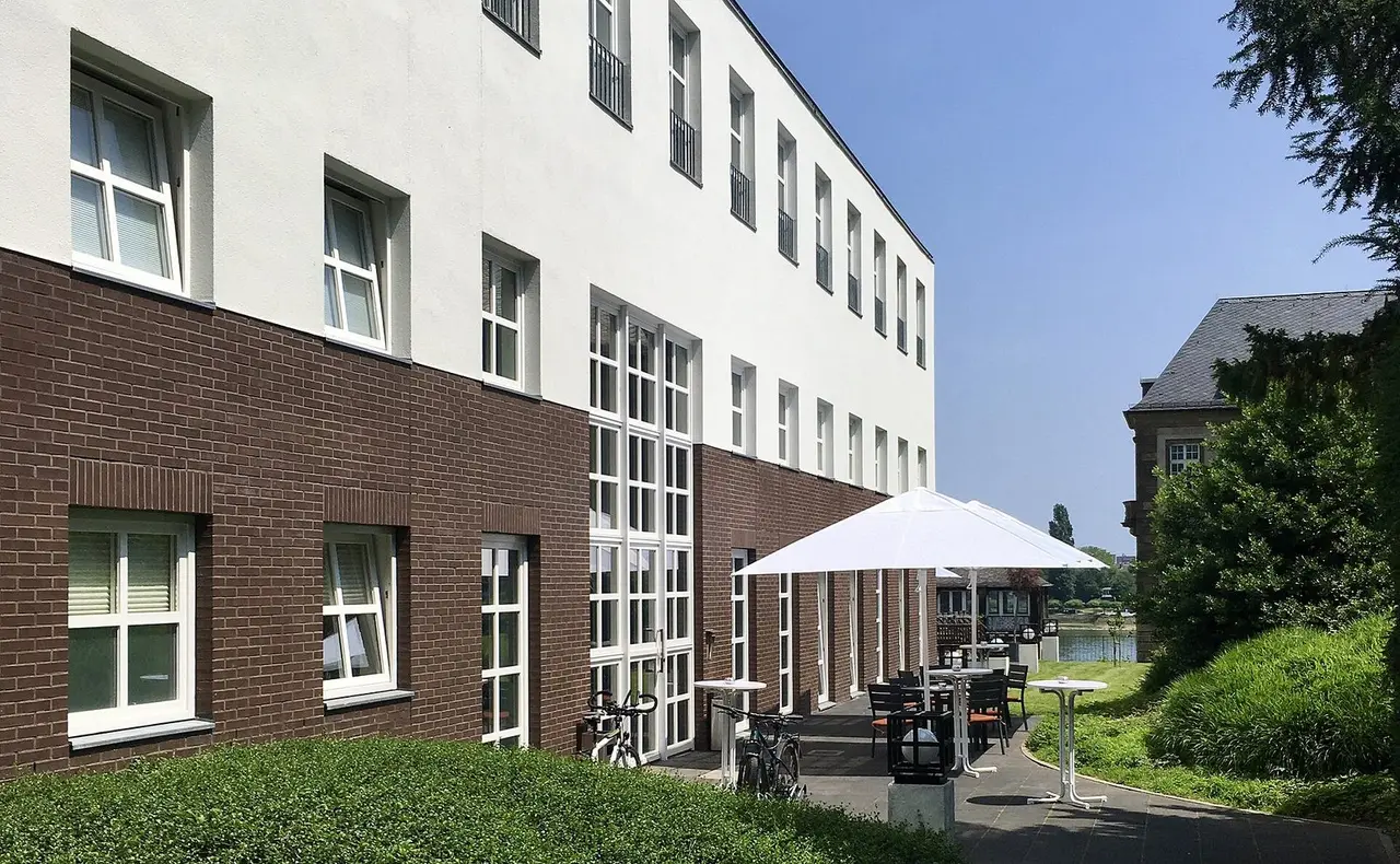 Backstein- und Putzfassade des Universitätsclubs Bonn mit Terrasse und Sonnenschirmen in Richtung Rhein
